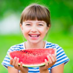 Mädchen mit Zahnspange isst ein Stück Wassermelone