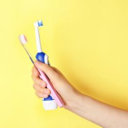 Handzahnbürste und elektrische Zahnbürste vor gelbem Hintergrund