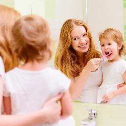 Mutter hilft Kleinkind beim Zähneputzen/Zahnseide und Mundwasser